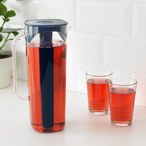 Una jarra de plástico transparente con un inserto negro que contiene un líquido rojo, probablemente té helado, y dos vasos llenos del mismo líquido rojo sobre una encimera blanca.