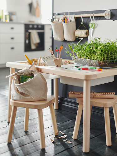 Mesa de juegos para niños con sillas de madera, con una planta, materiales de arte y organizadores colgantes.