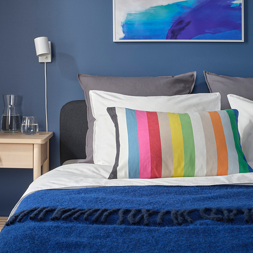 Cama con cojín de rayas multicolor BÄCKMÄRKEN, pared azul, estructura abstracta.