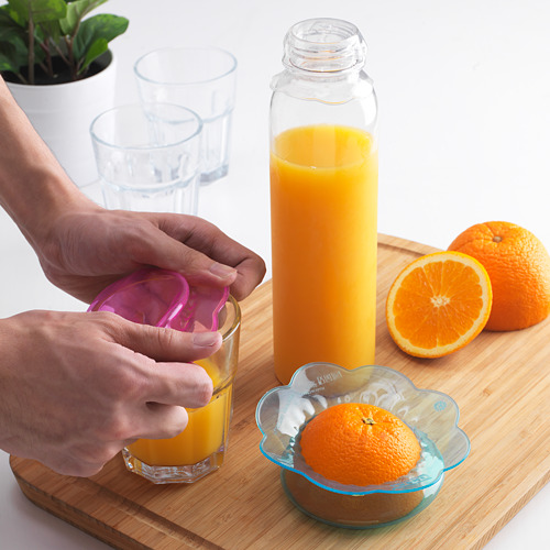 Una persona usa coloridas fundas de silicona para alimentos para sellar un vaso de jugo de naranja, manteniéndolo fresco.