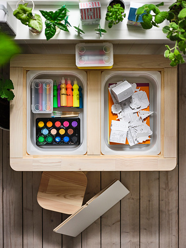 Caja de juguetes de madera con materiales de arte, estructuras de cartón y plantas.