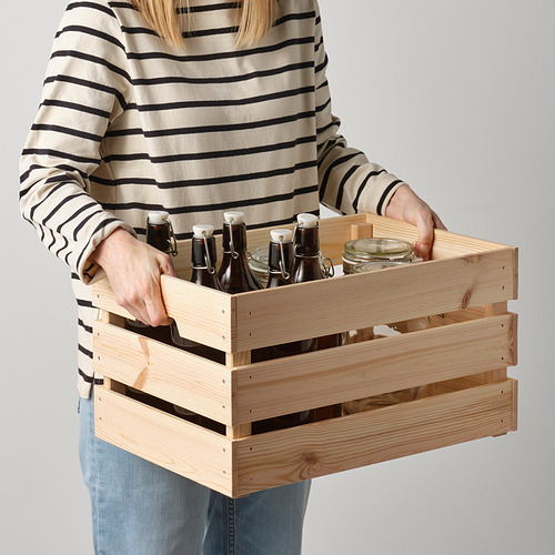 Una mujer sosteniendo una caja de madera con botellas. La caja tiene asas para facilitar la elevación.