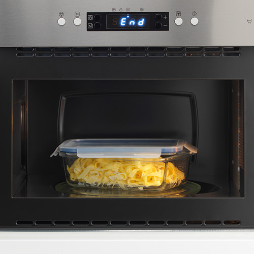 Un microondas con un recipiente de vidrio para alimentos apto para horno en su interior, calentado, con una tapa transparente y una función de cierre a presión.