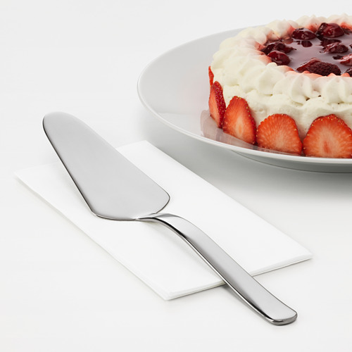 Cortadora de tartas de acero inoxidable junto a una tarta de fresas con nata montada. Parte de la serie IKEA 365+, diseño simple y duradero.