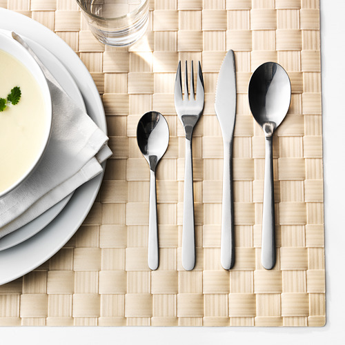 Una mesa con un plato de sopa, una pila de platos blancos y un juego de cubiertos de acero inoxidable pulido dispuestos sobre un tapete beige texturizado.