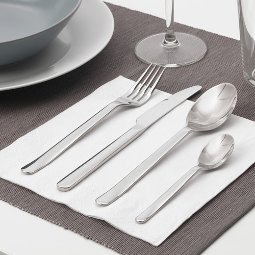 Una mesa cuidadosamente dispuesta con tenedor, cuchillo, cuchara, cuchara sobre una servilleta blanca sobre un mantel individual gris, junto con un tazón, un plato y una copa de vino.