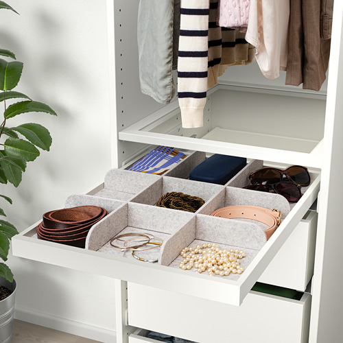 Cajón organizado con compartimentos de fieltro para cinturones, joyas y accesorios en un armario blanco.