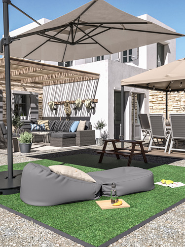 Patio trasero con bordes grises RUNDEN, césped artificial, mesa de picnic y muebles de patio bajo sombrilla beige.