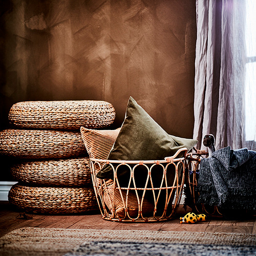 Acogedor rincón con taburetes de mimbre, almohadas de olivo y cesta decorativa.