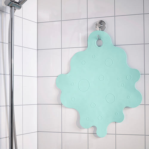 Una alfombra de baño antideslizante de color verde claro cuelga de una pared de ducha de azulejos blancos. Las ventosas lo aseguran en su lugar por seguridad.