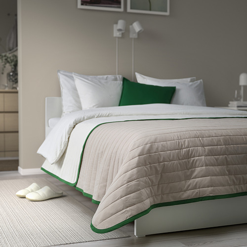 Colcha acolchada blanca y verde con cenefa en cama grande, con zapatillas.