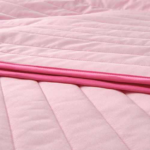 Primer plano de una suave colcha acolchada de color rosa con borde rosa oscuro, que muestra detalles de costuras y textura.