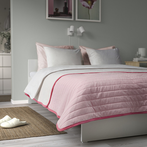 Cama cuidadosamente hecha con colcha rosa / blanca VETEJORDFLY, almohadas equilibradas y zapatillas blancas al lado.