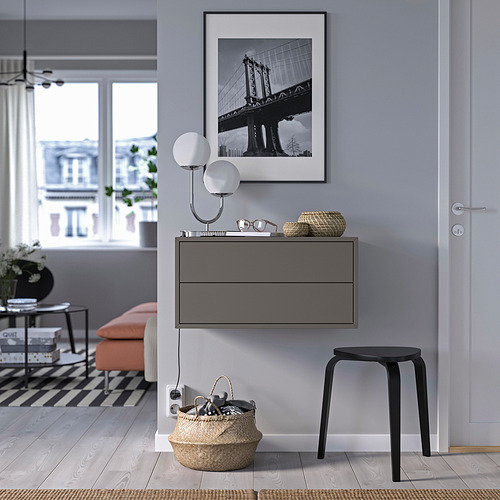 Habitación moderna: bridge art con marco negro, lámpara de pared, armario gris con cajones, banco naranja, taburete negro, cesta grande con llaves.