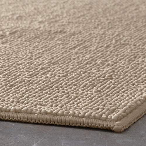 Alfombrilla de baño beige texturizada con patrón de puntos en relieve y bordes cosidos.