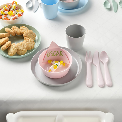 Una mesa para niños con platos coloridos, cubiertos y bocadillos. Los platos están apilados y un tazón pequeño contiene una servilleta con el nombre de Oscar.
