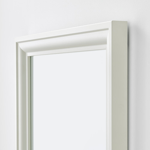 Un espejo con marco blanco y un diseño elegante, colocado verticalmente, contra una pared lisa.
