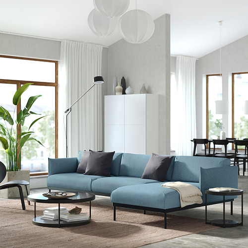 Sala de estar moderna con sofá azul ÄPPLARYD, elegantes cojines, elegantes mesas de café, grandes ventanales y plantas de interior altas.
