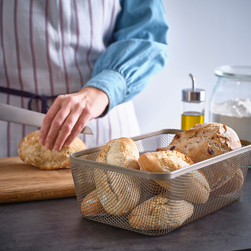 Una persona mete la mano en una cesta de almacenamiento IKEA 365+ de malla llena de hogazas de pan, mostrando su diseño transpirable para el almacenamiento de alimentos.