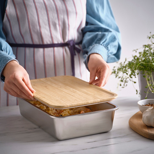 Persona colocando una tapa de bambú en un recipiente de acero inoxidable para alimentos en la encimera de la cocina.