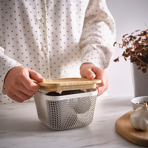 La persona coloca una tapa de bambú en la canasta de ikea con ajo y planta.