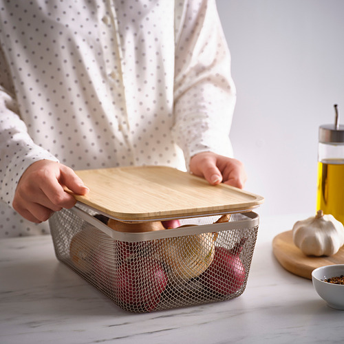 La persona coloca una tapa de madera en la canasta de almacenamiento de malla que contiene frutas, lo que promueve la circulación del aire y el almacenamiento a temperatura ambiente.