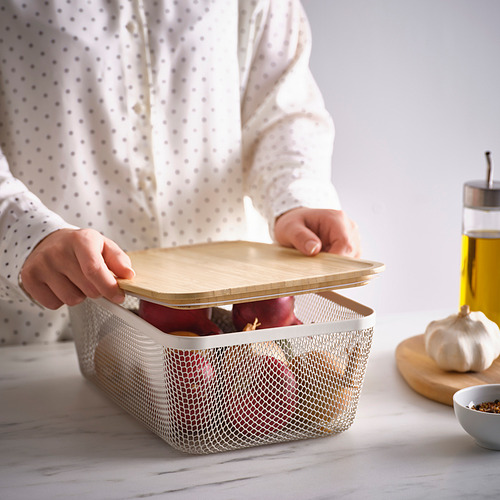 Una persona levanta una tapa de bambú de una cesta de almacenamiento de malla IKEA 365+ llena de manzanas sobre una mesa.