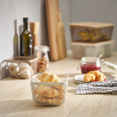 La cesta de malla blanca IKEA 365+ contiene croissants, pequeños, se sientan en una mesa de madera con varios artículos de cocina.