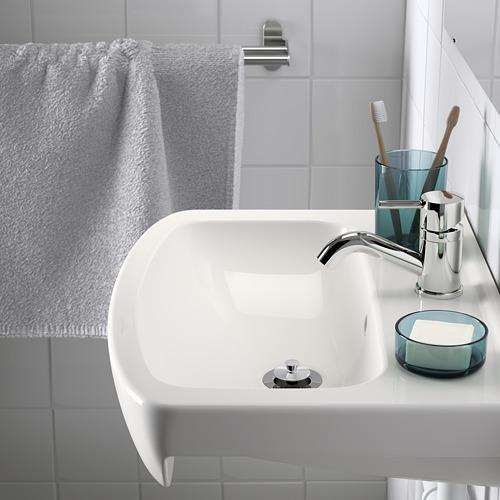 Fregadero de pared blanco con grifería cromada y accesorios azul grisáceo. La toalla cuelga a la izquierda.