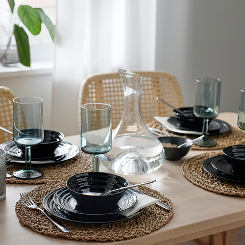 Mesa de comedor con cristalería negra, vasos azules verdosos y manteles individuales. Decantador centrado para servir.