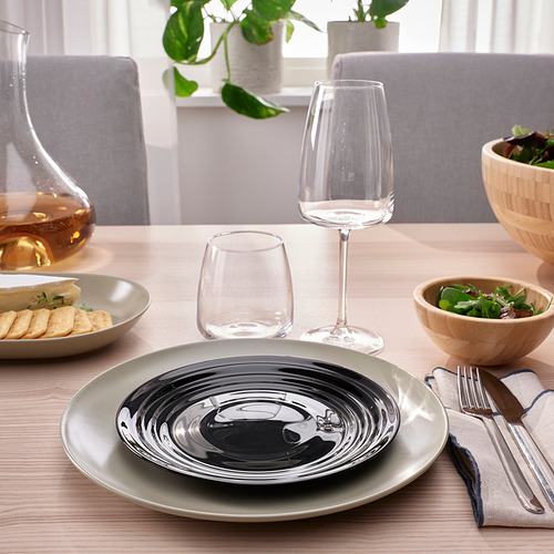 Plato blanco y negro, copas de vino, queso y galletas, verduras en mesa de madera.