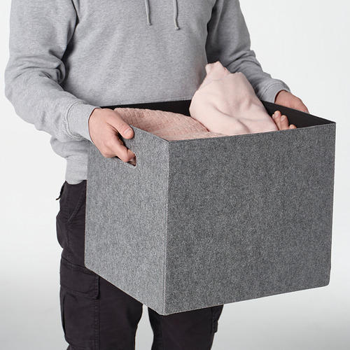 Persona que sostiene una caja de fieltro gris con asas, diseñada para adaptarse a las estanterías kallax.