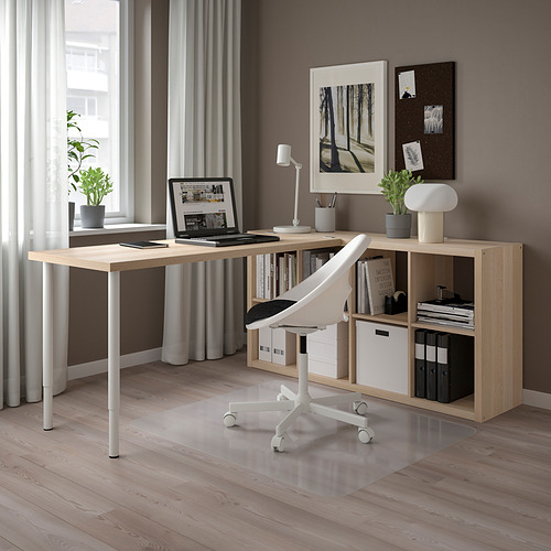 Moderna configuración de escritorio en forma de L de madera clara con silla blanca, computadora portátil, almacenamiento, plantas y obras de arte. Limpio, organizado y bien iluminado.