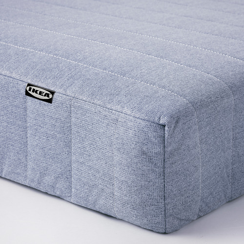 Primer plano de un firme colchón gris de IKEA con costuras y etiqueta visibles.