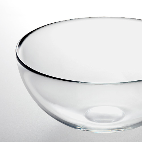 Cuenco de vidrio transparente con diseño liso y sencillo, que refleja la luz en el borde, colocado sobre una superficie blanca.