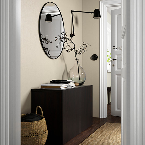 A modern entryway with a black BESTÅ sideboard, mirror, and lamps. A large basket sits beside it, leading to a bright white hallway.
