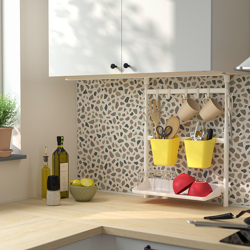 Cocina moderna con estante beige que sostiene utensilios, limones, vino y velas. Espacio acogedor y organizado con pared estampada y luz natural.