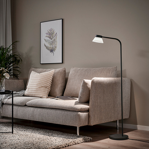 Salón moderno con lámpara de pie SAMBORD, sofá beige y póster vegetal. La lámpara al lado del sofá proporciona luz de lectura.