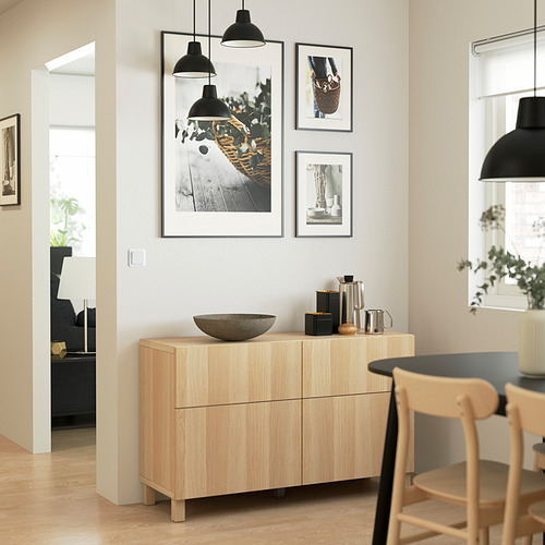 Sillas de madera y armario de colores claros junto a fotos enmarcadas y lámparas colgantes.