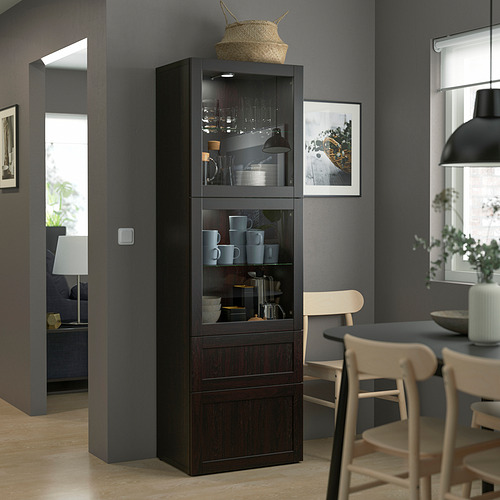 Armario de madera BESTÅ con puertas de cristal, utensilios de cocina, junto a sillas ligeras.