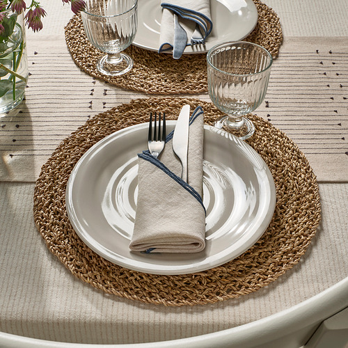 Mesa rústica con manteles individuales tejidos, platos blancos, servilletas dobladas y vasos.