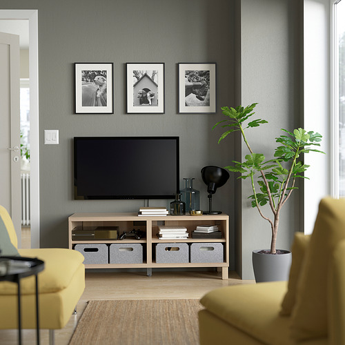 Sala de estar gris con banco de tv BESTÅ, pantalla plana, sillas amarillas, planta verde, lámpara negra y fotos sobre la televisión.