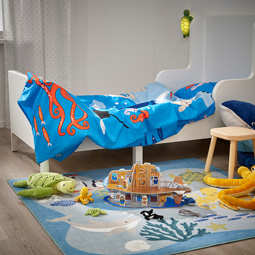Tortuga verde BLÅVINGAD juguete sobre alfombra azul, manta de pulpo, cama blanca, taburete de madera, decoración de criaturas marinas.