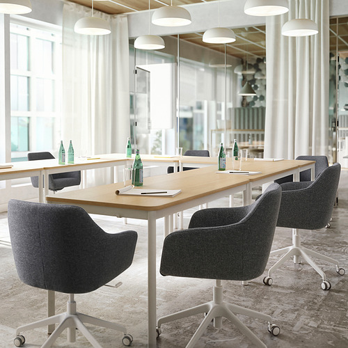 Moderna sala de reuniones con sillas giratorias grises, mesas de madera, papeles y luz natural.
