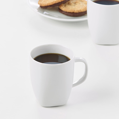 Dos tazas blancas de café junto a un plato de galletas. Tazas de porcelana feldespato duradera y resistente a los impactos.