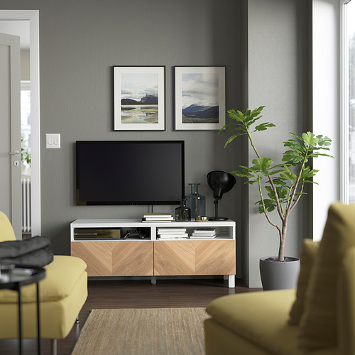 Modern living room: BESTÅ tv stand in white/beech, holding tv. Yellow chairs, gray wall, plant. Photos, lamp, books on stand.