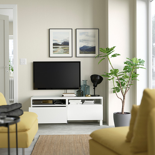 Sala de estar moderna con mueble de TV BESTÅ, TV de pantalla plana, fotos de montaña, sillas amarillas, plantas, texturas.