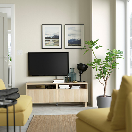 Sala de estar moderna con mueble de televisión BESTÅ, sofás amarillos, plantas de interior y estampados de la naturaleza.