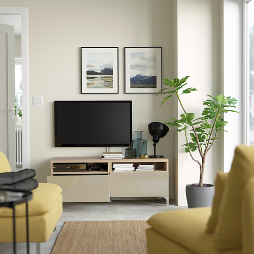 Sala de estar con sofá amarillo, televisor de pantalla plana, banco de televisión NANNARP, dos fotos de montaña enmarcadas y una planta en maceta.
