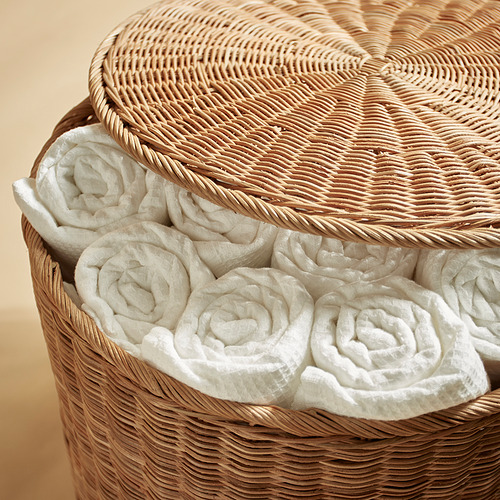 Cesta tejida de ratán natural, rellena de toallas blancas cuidadosamente enrolladas, que muestra la artesanía de calidad y la solución de almacenamiento.
